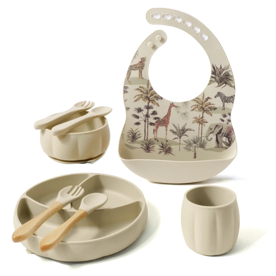 Children's dining set with bowl, cup, plate, and bib featuring animal patterns on a white background.