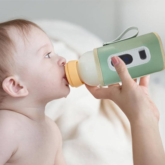 Baby drinking from a green and orange baby bottle held by an adult.