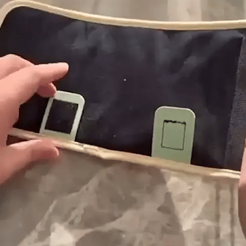 Hand holding a black bag with green straps against a neutral background