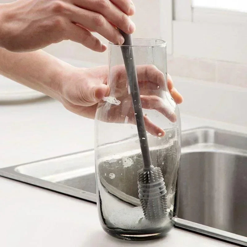 Person cleaning a glass bottle with a brush in a kitchen setting