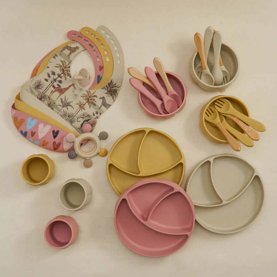Collection of children's tableware including plates, bowls, and utensils on a light background