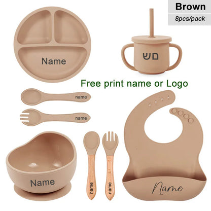 Set of brown baby utensils including plate, cup, bowl, spoons, and bib with customizable name or logo.