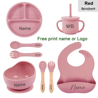 Pink children's dining set with various items including a bowl, cup, spoon, and bib on a white background.