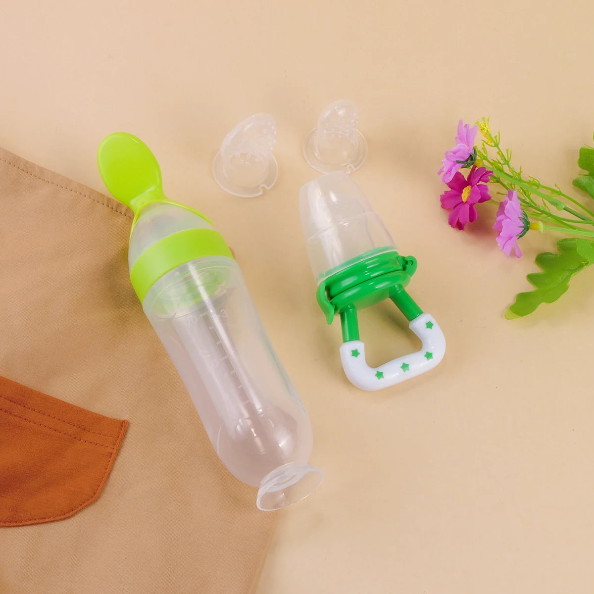 Two green and clear baby feeders on a beige background with flowers.