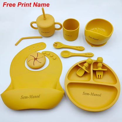 Yellow children's dining set including cup, bowl, spoon, fork, bib, and plate on a white background.