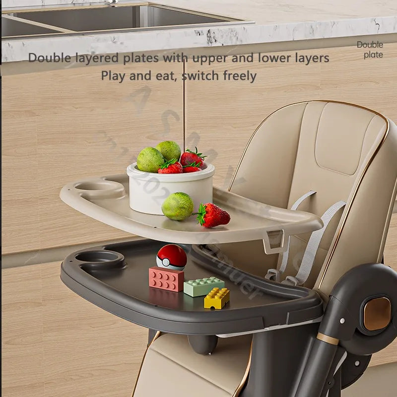 High chair with a double-layered tray containing fruits, toys, and a bowl in a kitchen setting.