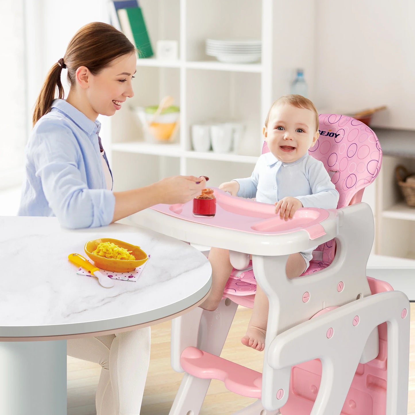 Woman and baby using a pink and white high chair at a dining table.