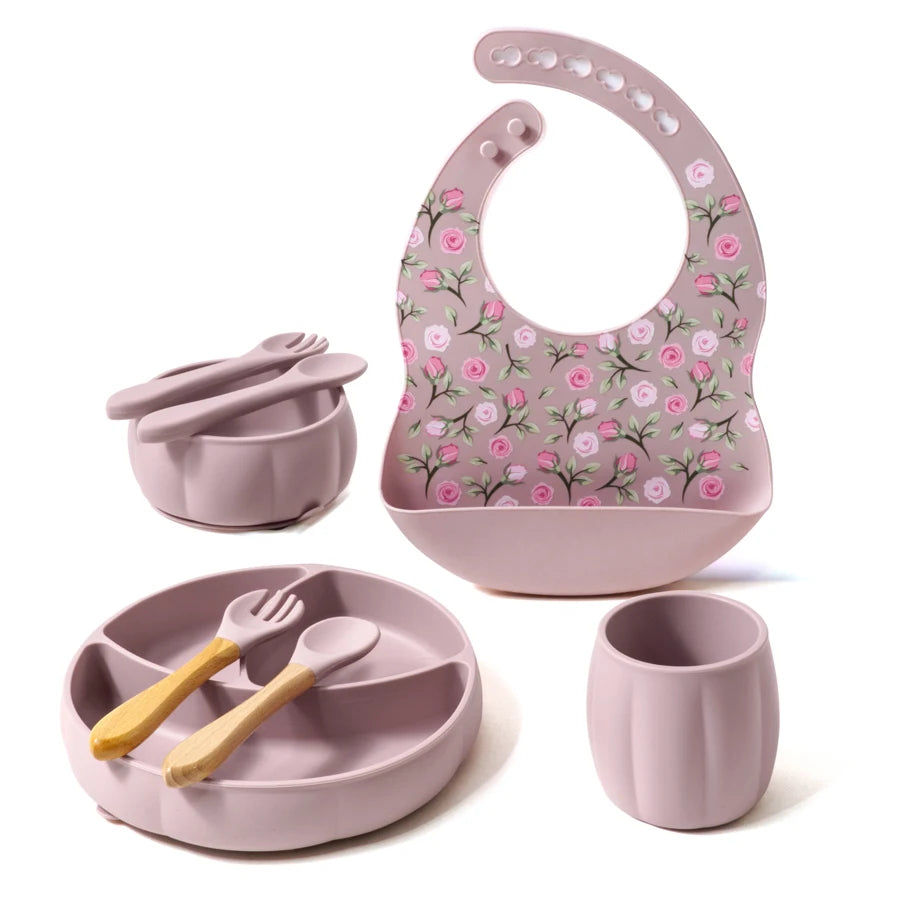 Children's dining set with pink bib, plate, cup, and utensils on a white background