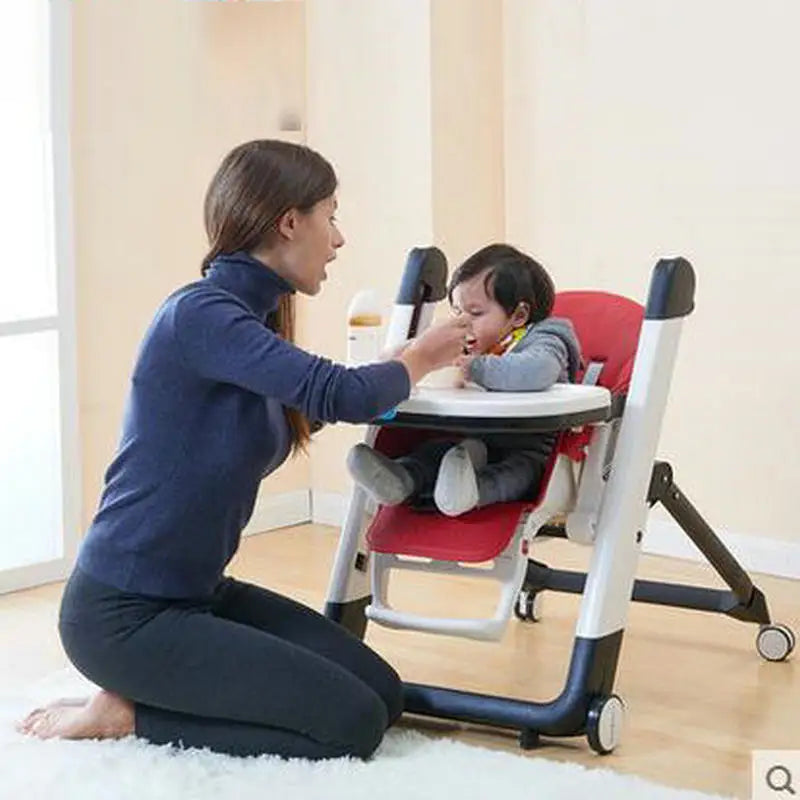 Woman feeding a child in a red and white high chair in a home setting.