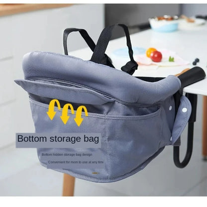 Gray baby seat with a bottom storage bag feature, placed on a table.